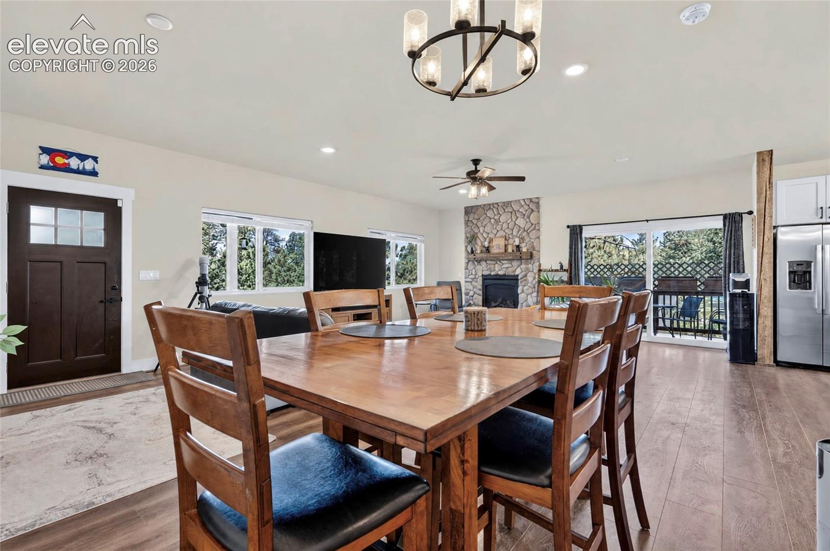 Open-concept interior featuring wood-finish flooring, a floor-to-ceiling stone fireplace with a timber mantel, recessed lighting, and a chandelier