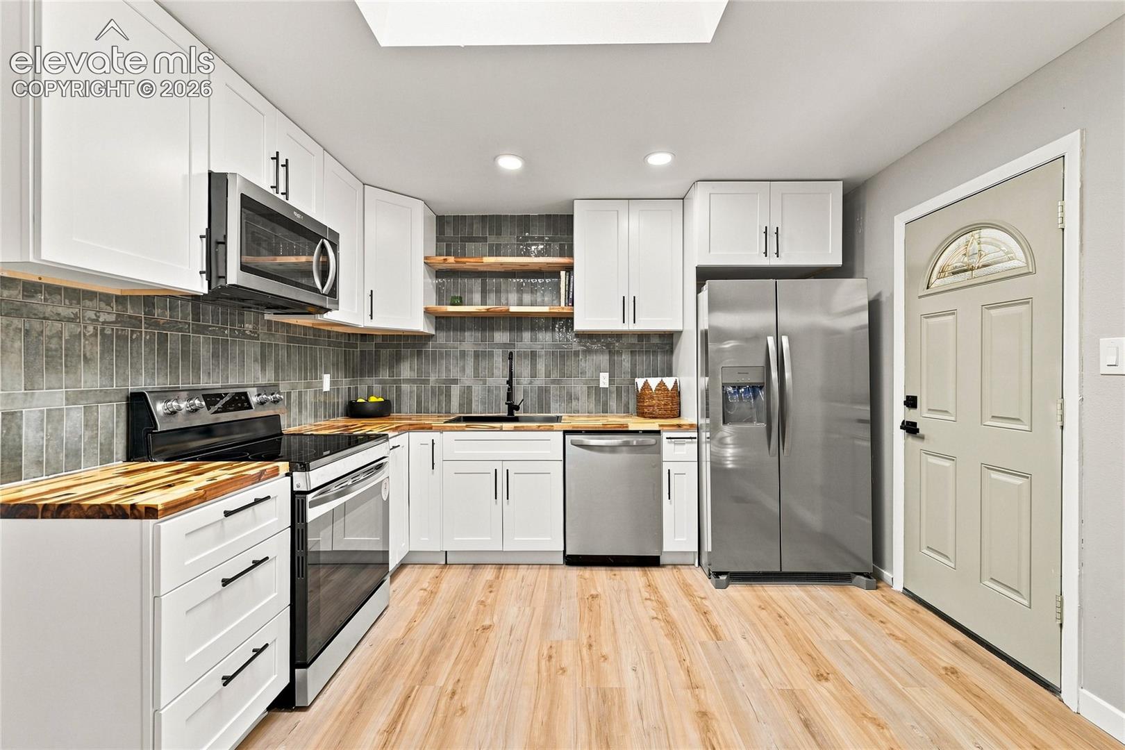 Kitchen featuring light wood-finish flooring, white cabinetry with black hardware, stainless steel appliances, wood countertops, and a skylight
