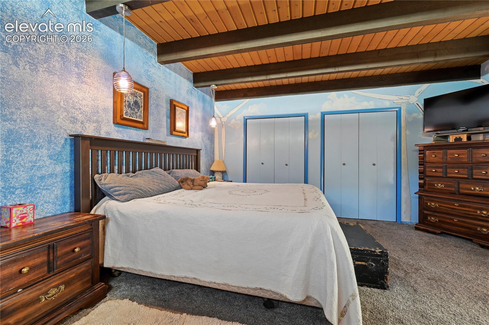 Main Bedroom, Vaulted wood-paneled ceiling with exposed beams, textured blue accent wall, two sets of white bifold closet doors, and recessed lighting