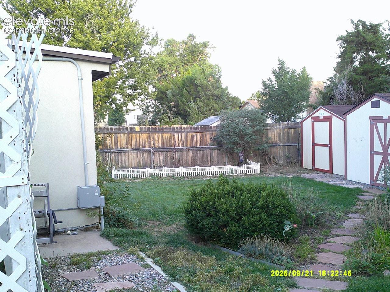 Expansive backyard featuring a privacy fence, two storage sheds, a stone pathway, and mature landscaping