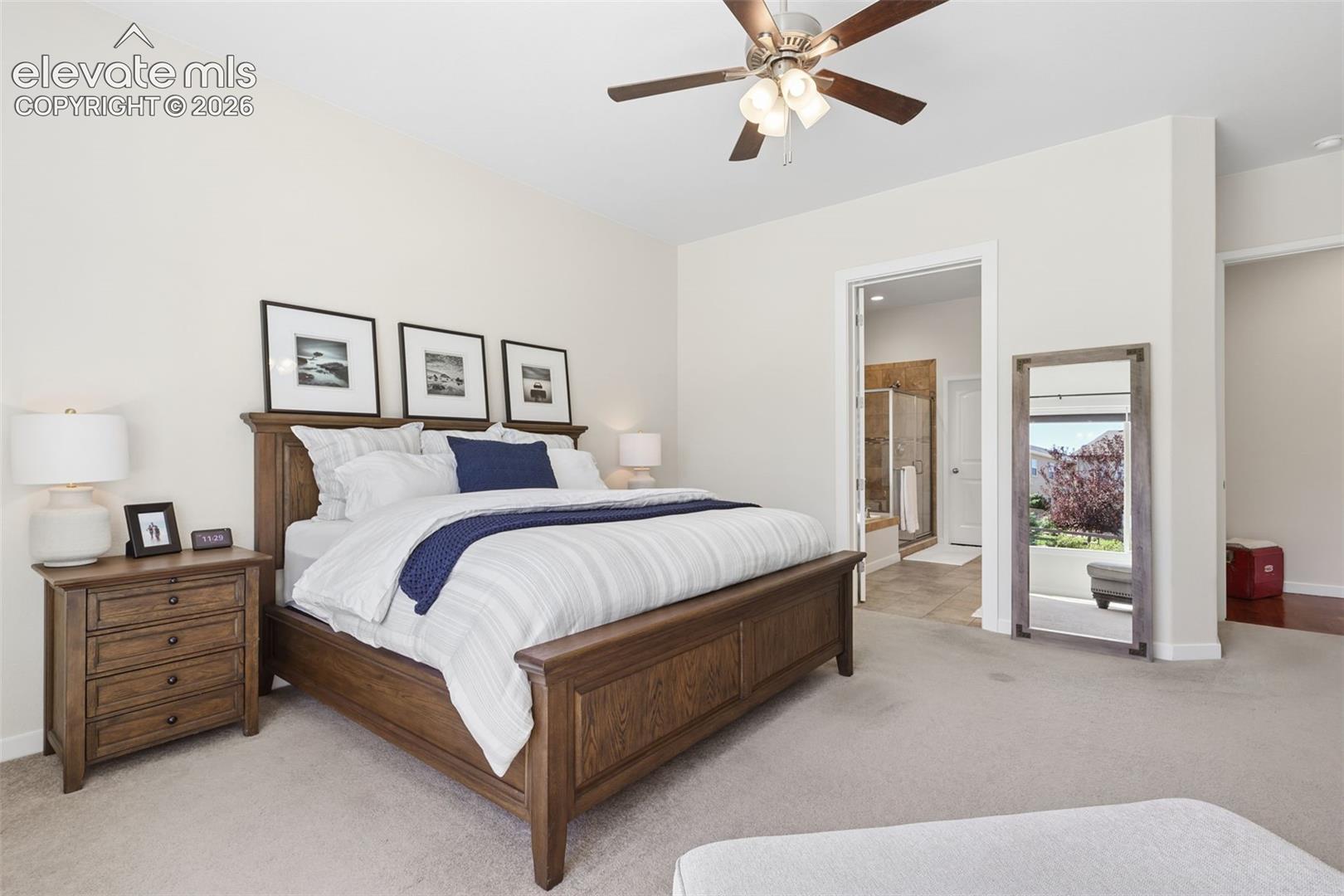 Carpeted flooring, ceiling fan, neutral wall tones, hardwood furniture, and an en-suite bathroom entry