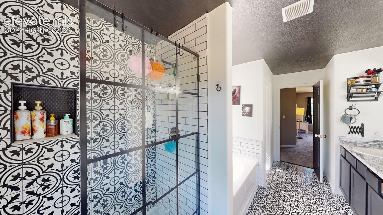 Patterned floor tiling, glass-enclosed shower with black grid accents, subway tile shower walls, built-in shower niche, and a vanity with an integrated sink