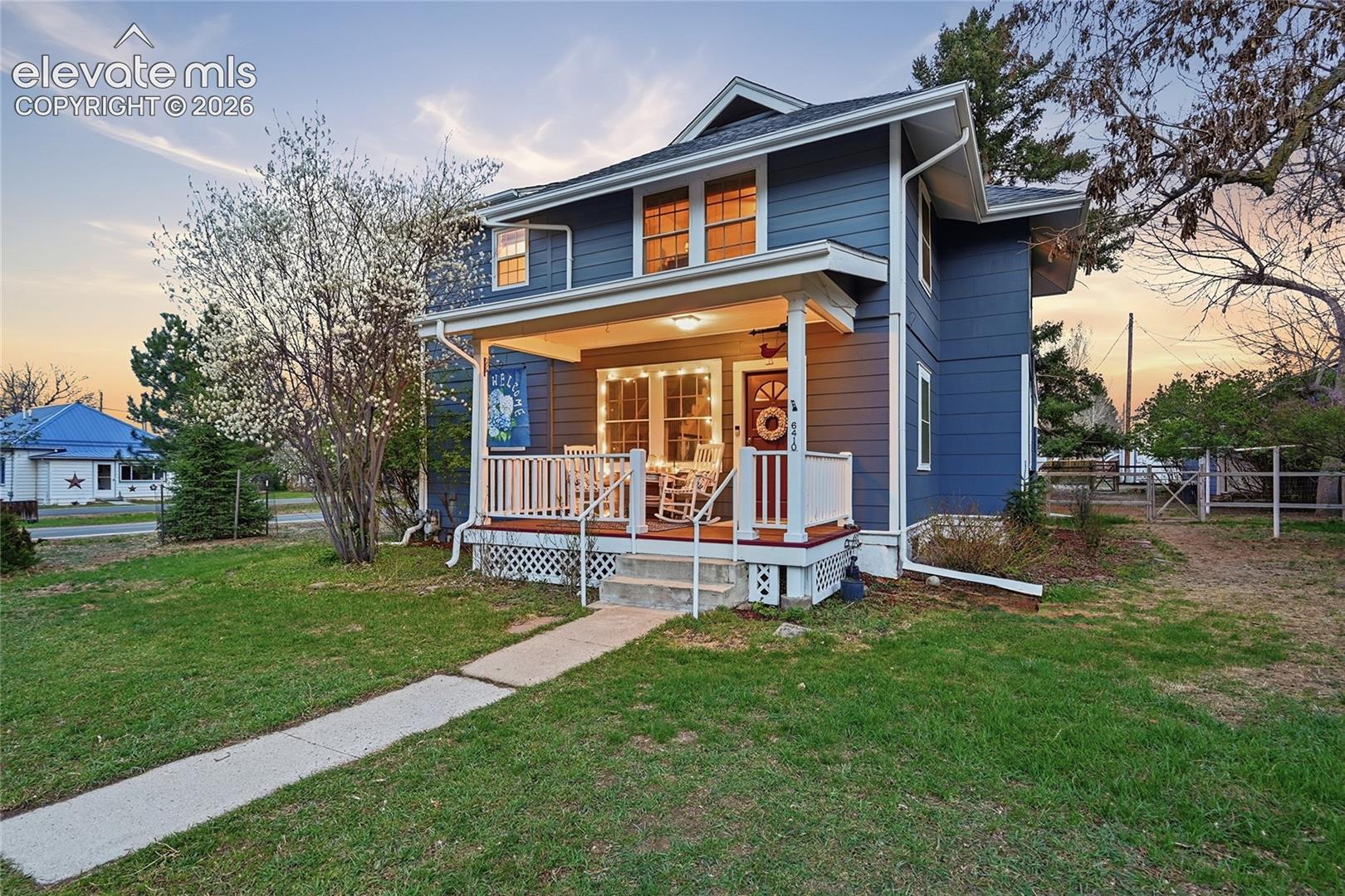 Two-story exterior featuring blue horizontal lap siding, a covered front porch with white railings, and a concrete walkway