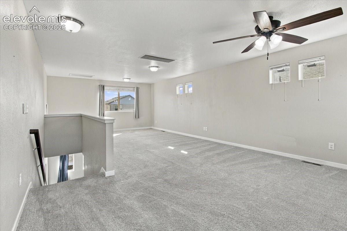 Spacious carpeted room featuring multiple windows, a ceiling fan, and recessed lighting