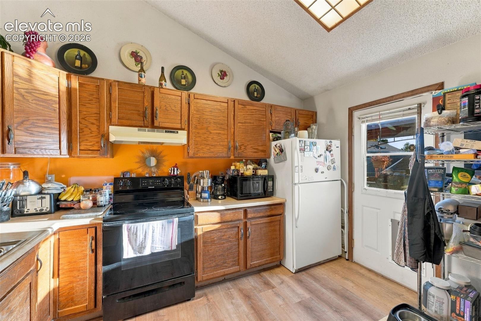 Kitchen featuring wood cabinetry, solid-surface countertops, vaulted ceiling, wood-finish flooring, and a glass-paneled exterior door