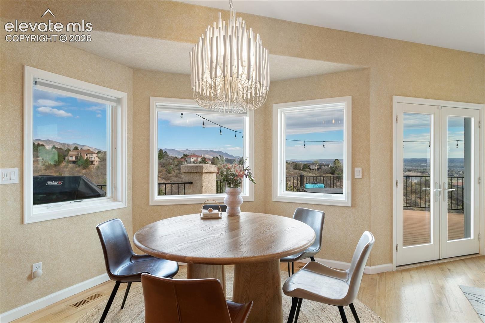 Dining area featuring a contemporary chandelier, multiple windows with mountain scenery, French doors accessing a deck, light wood-finish flooring, and textured wall finishes