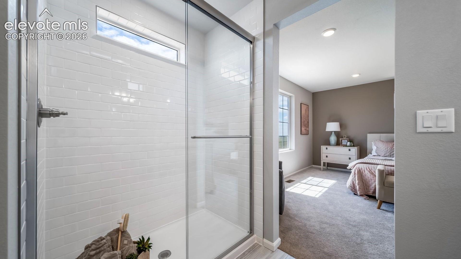 Shower enclosure featuring white subway tile surround, clear glass door, and a transom window
Photos of a model home
