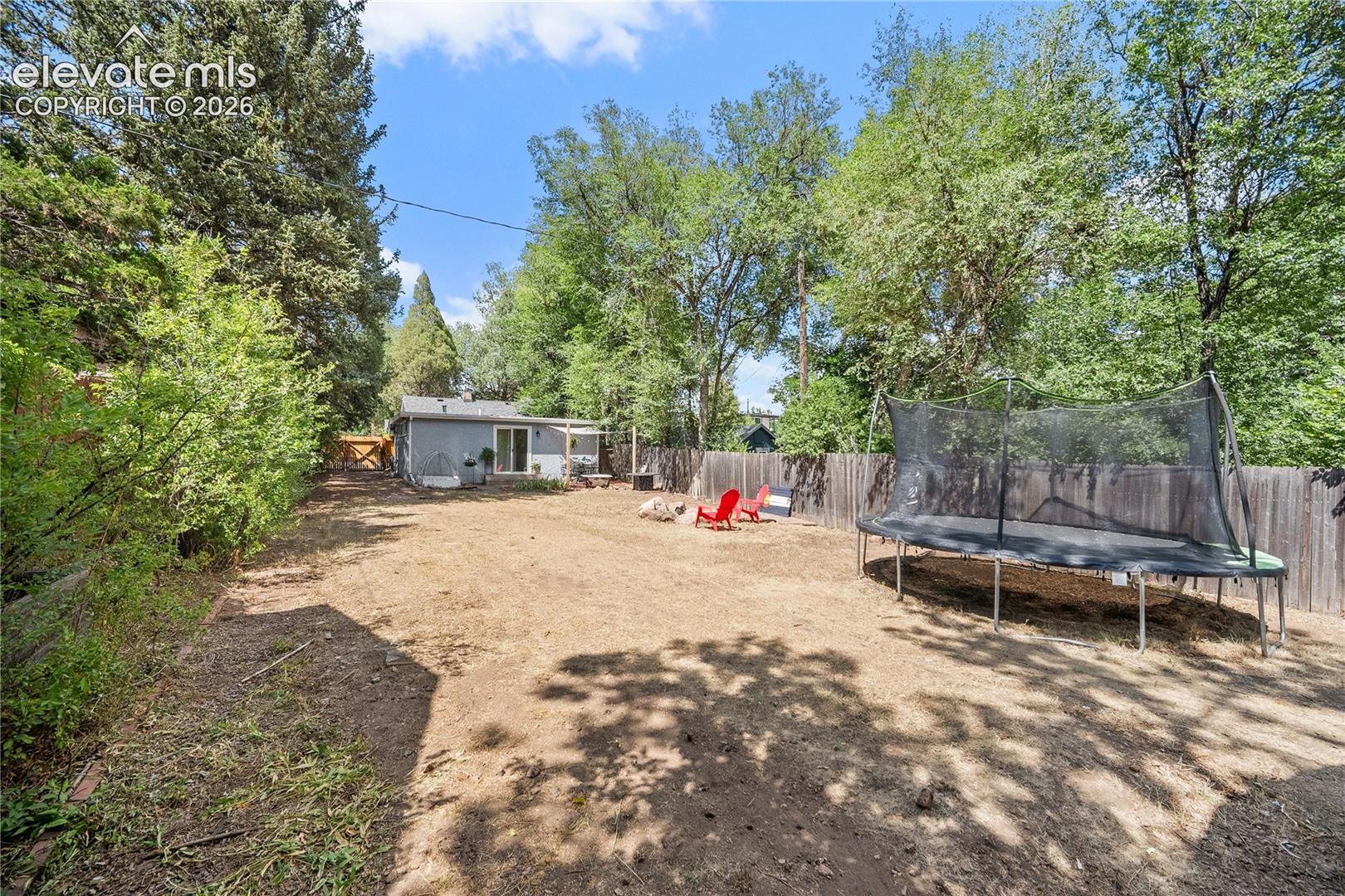 Expansive backyard featuring a privacy fence, mature trees, and a fire pit area