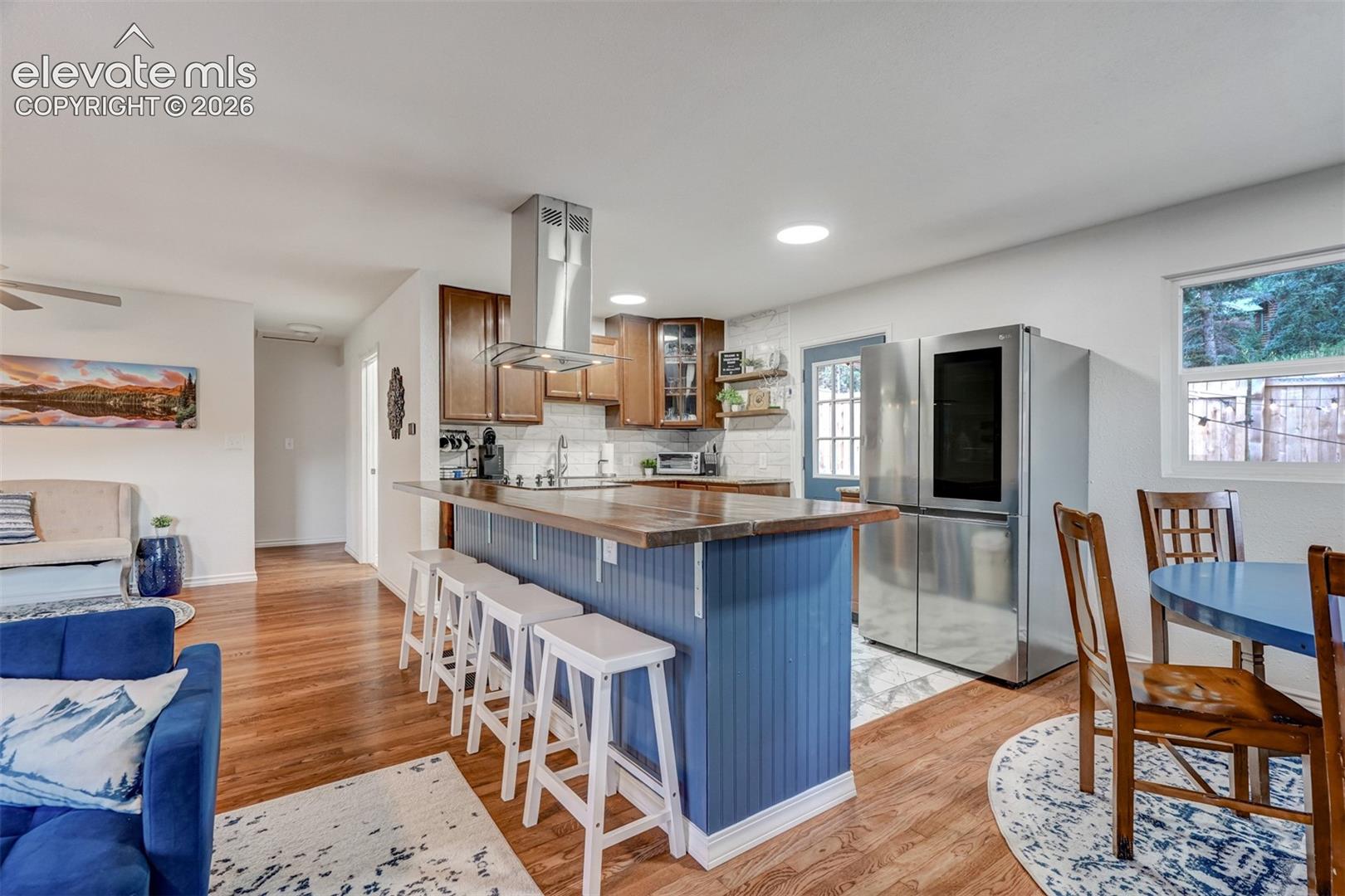 Kitchen island with wood-finish countertop, stainless steel range hood, and tile backsplash