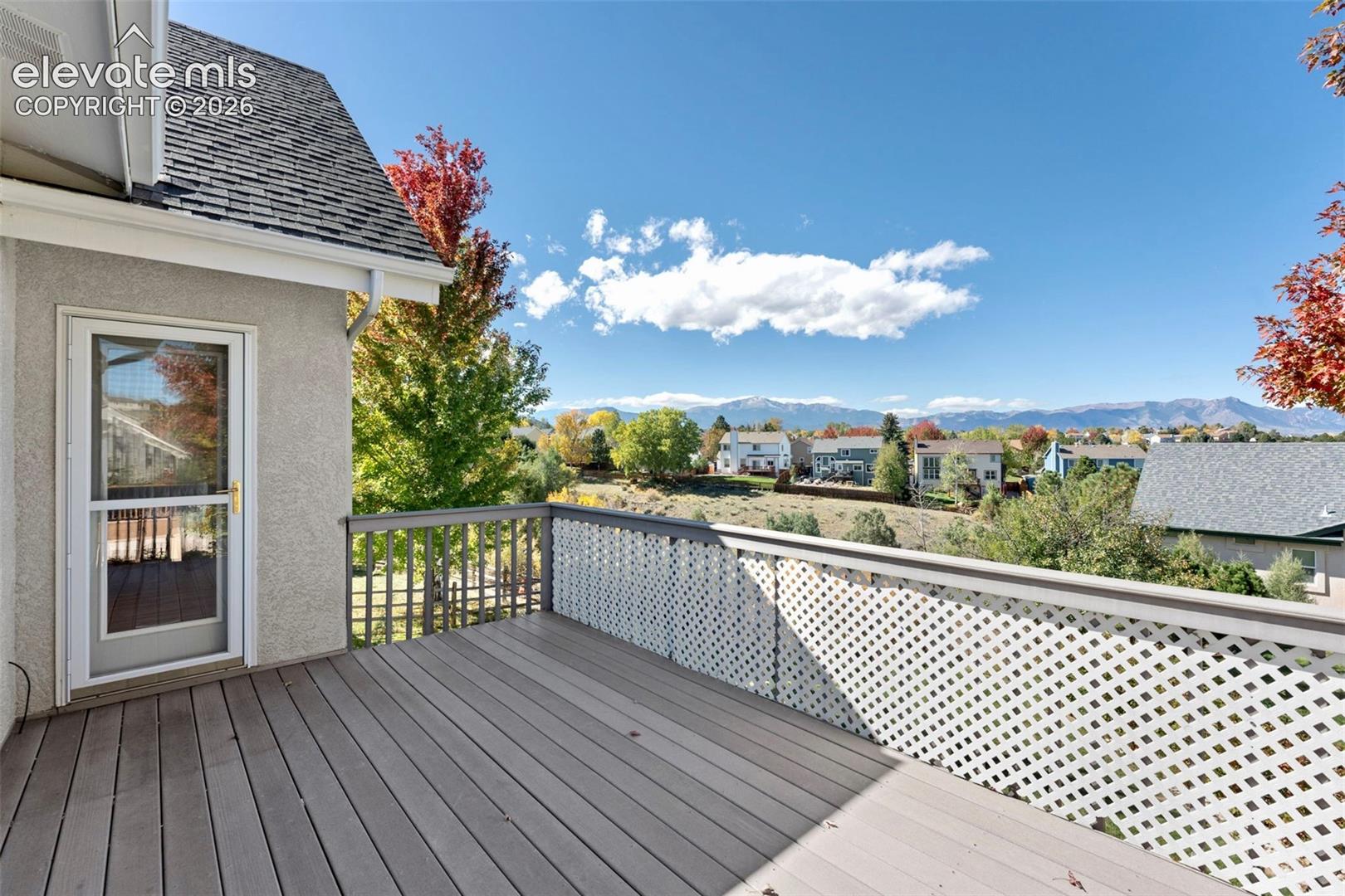 Elevated deck featuring wood-finish decking, white lattice railing, and mountain backdrop