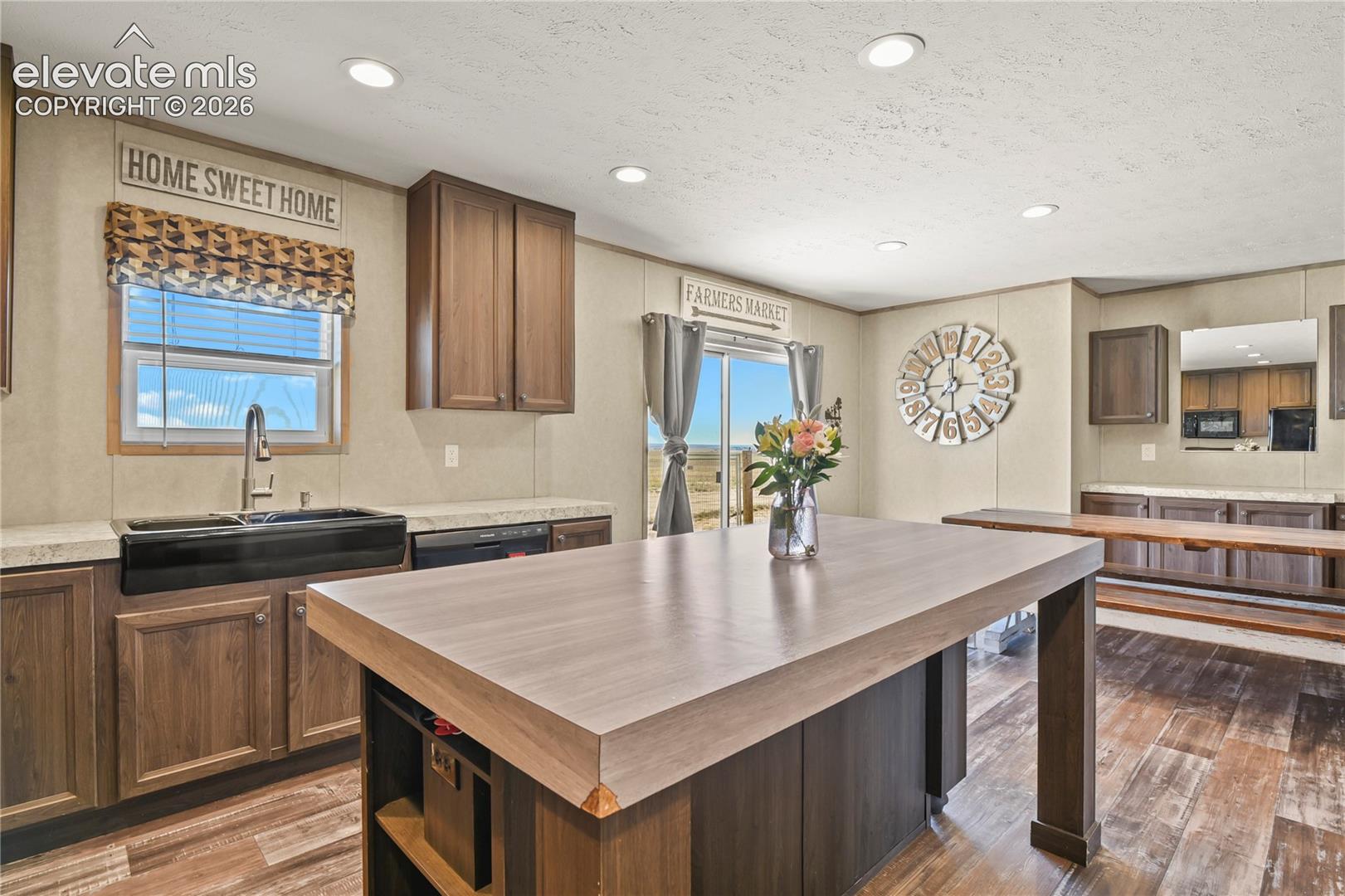 Kitchen featuring a central island with a wood-finish countertop, dark wood-tone cabinetry, recessed lighting, and a black farmhouse-style apron sink with a gooseneck faucet