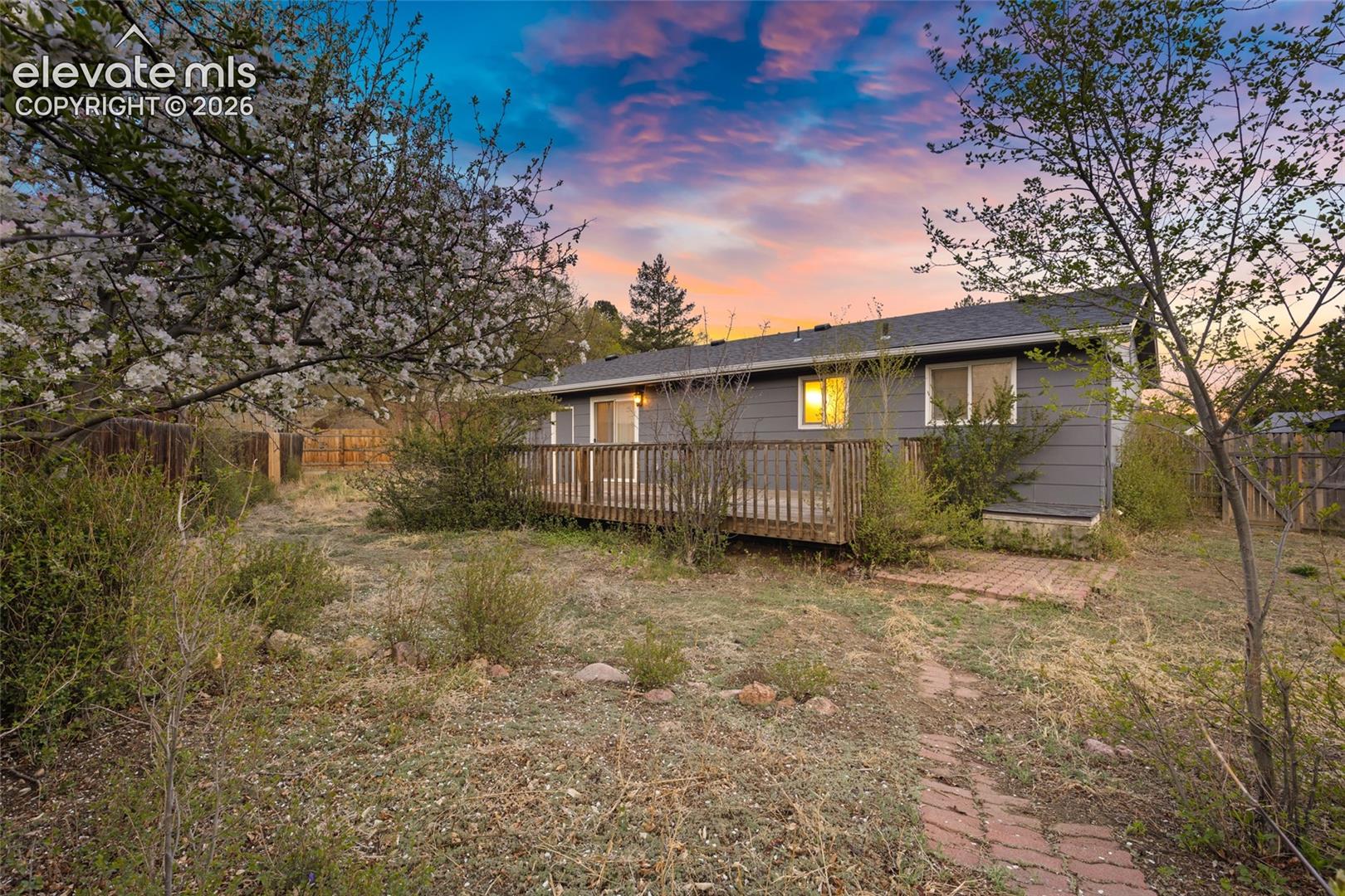 Rear exterior featuring a wooden deck, sliding glass doors, and a brick pathway