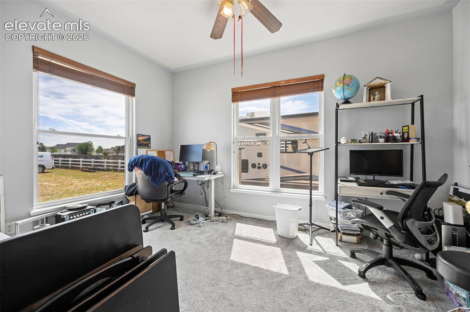 Carpeted room with light gray walls, two large windows with horizontal blinds, and a ceiling fan with integrated lighting