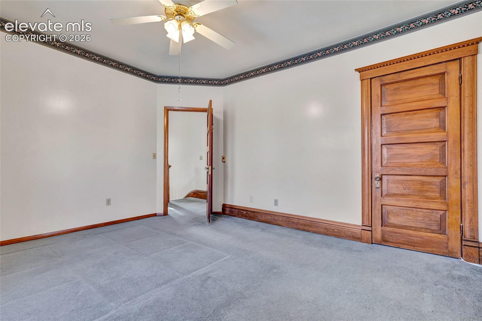 Room featuring natural wood-finish five-panel doors, matching wood-finish trim, ceiling fan with light fixture, and decorative wall border