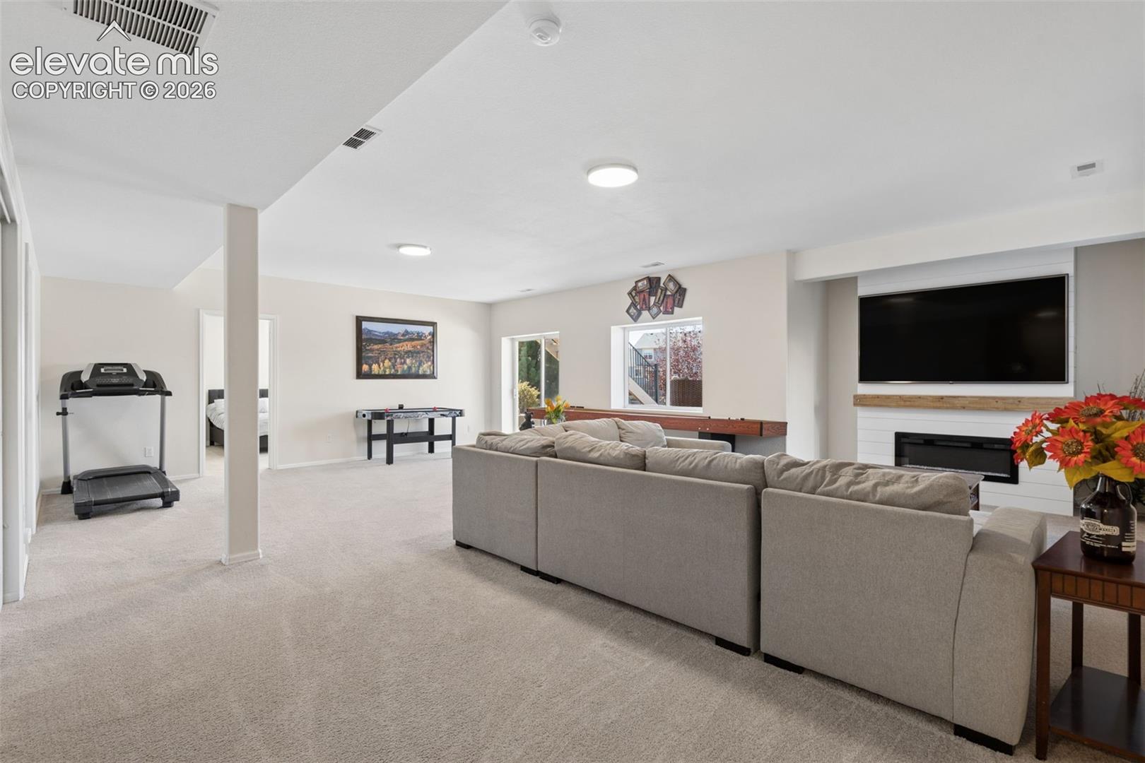 Spacious living area featuring light-colored carpeting, a modern electric fireplace with a wood mantel, and sliding glass door access to back yard
