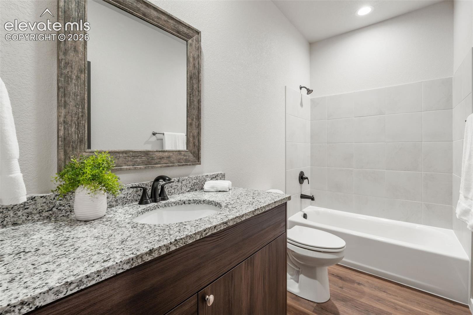 Bathroom featuring a vanity with stone-finish countertop, undermount sink, matte black fixtures, framed mirror, and wood-finish flooring