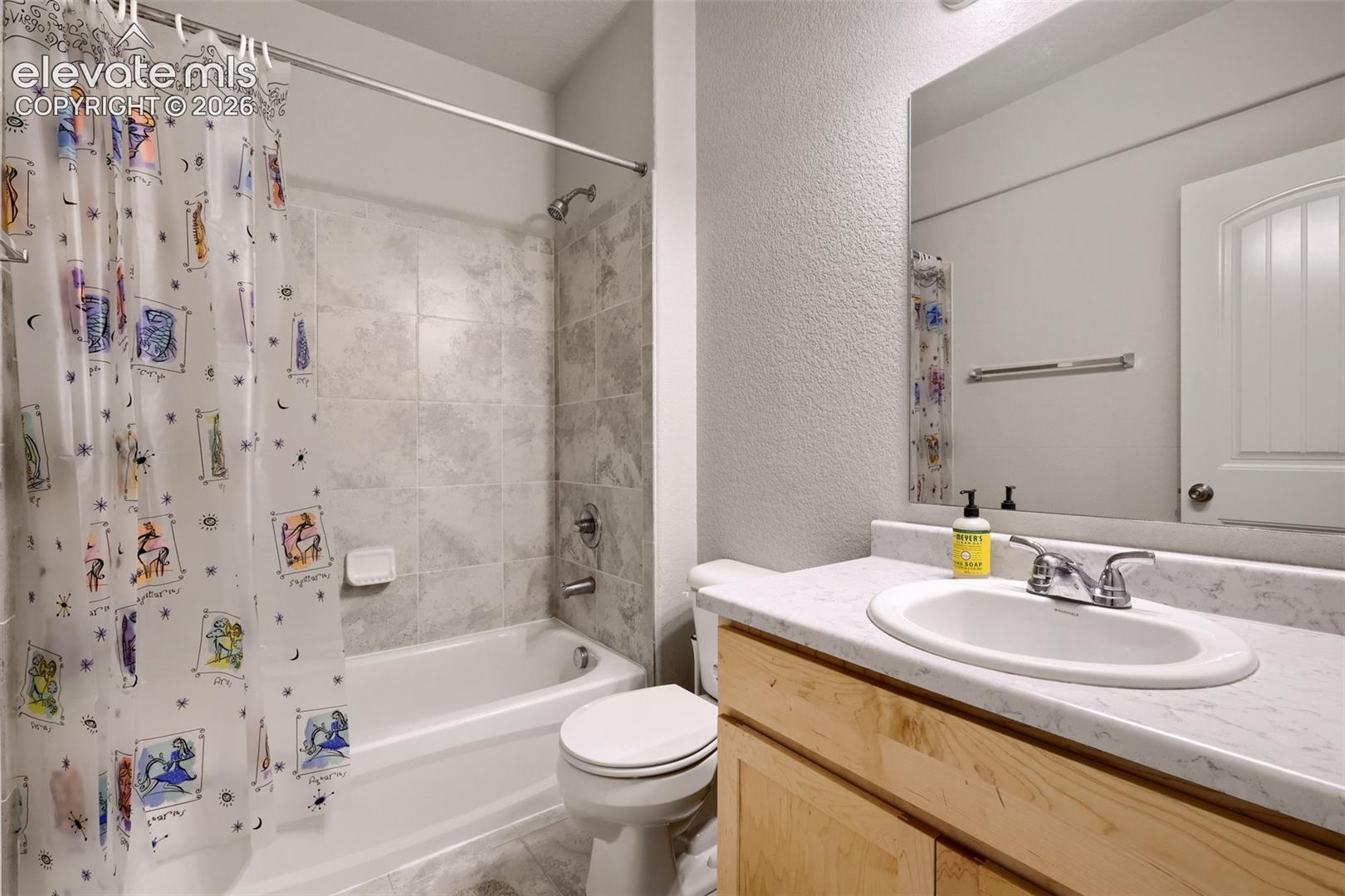 Tub and shower combination with light-toned tile surround, single vanity with light countertop, and wood-finish cabinetry
