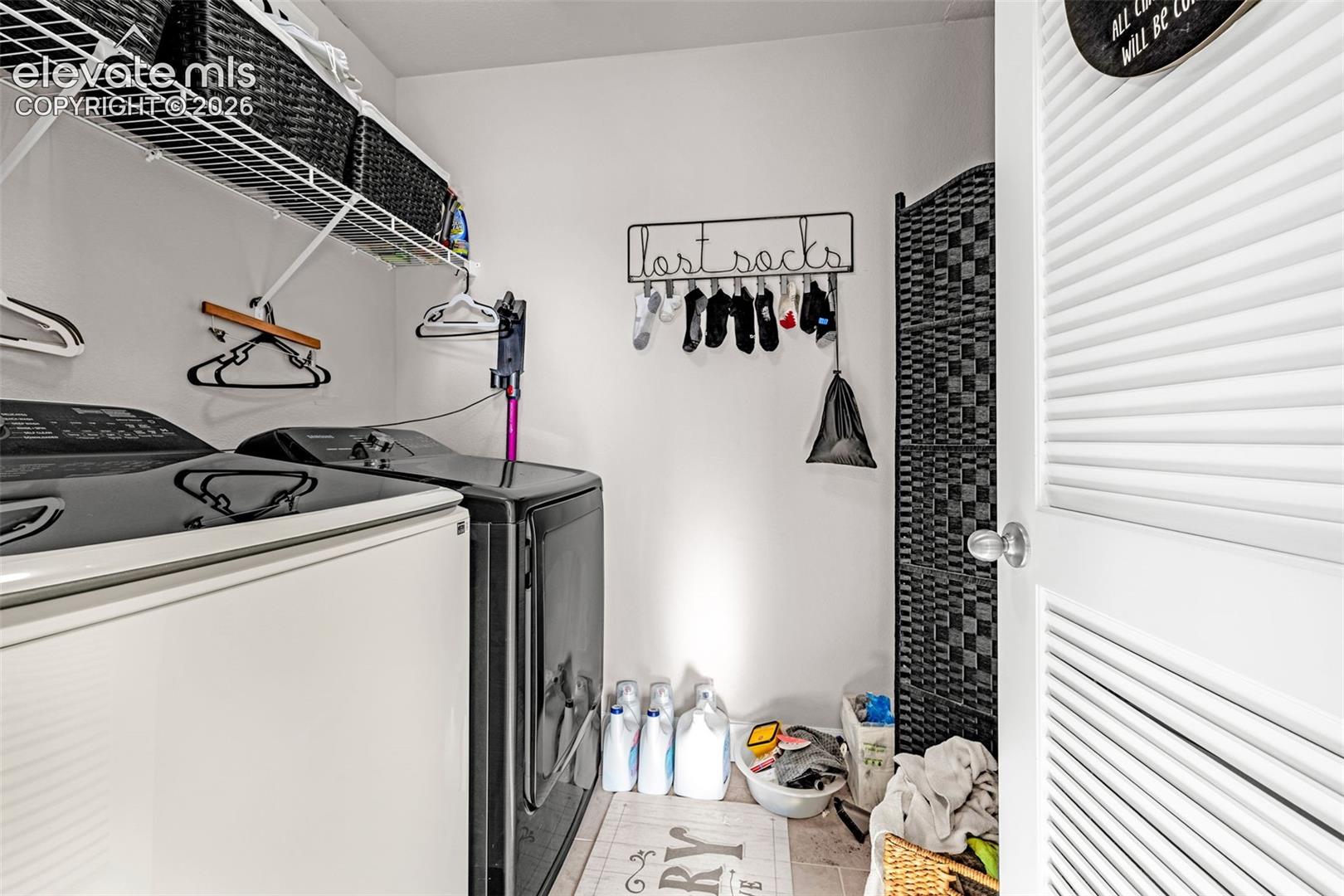 Dedicated laundry space featuring a white louvered door, tile flooring, and integrated wire shelving