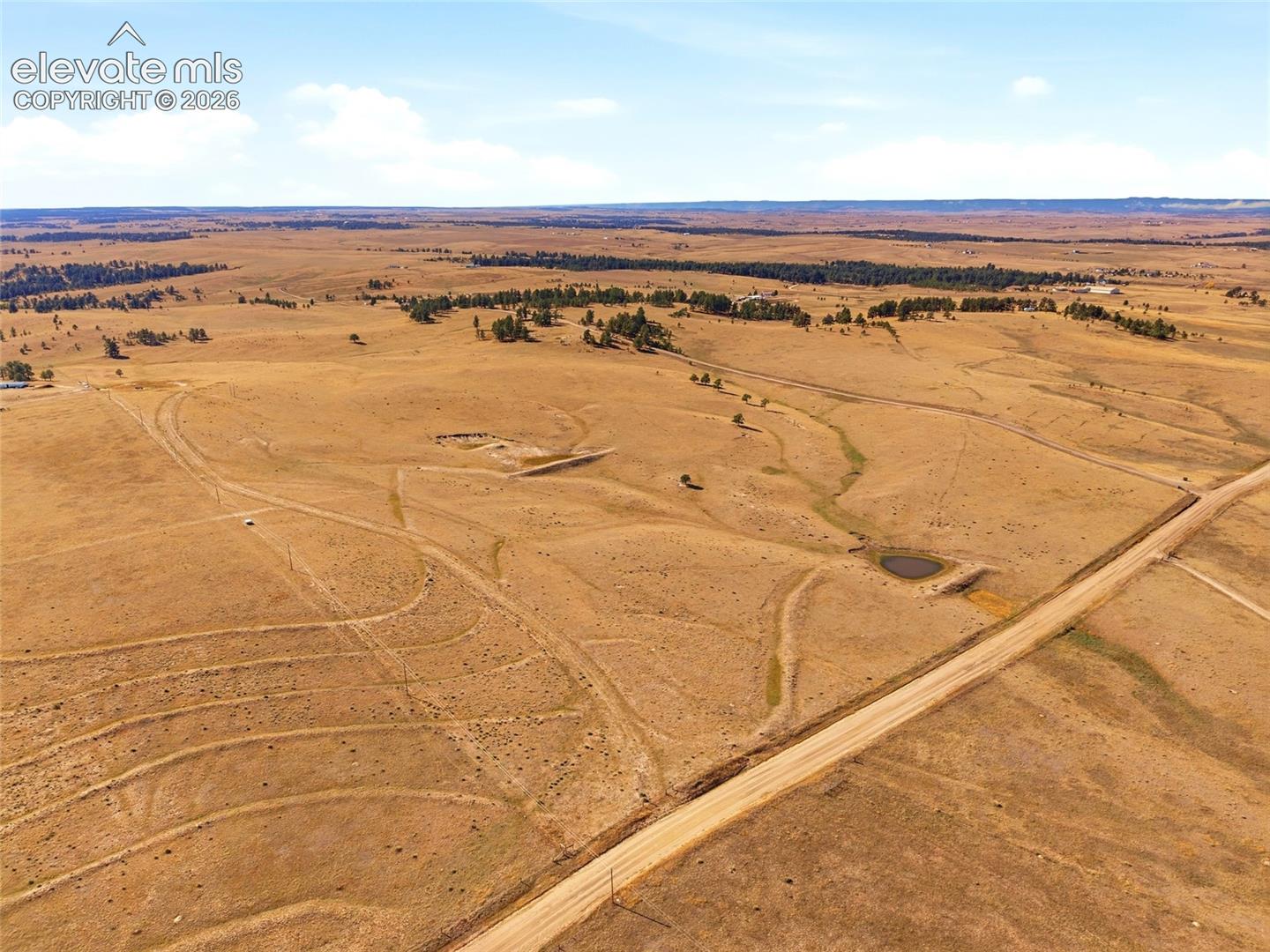 Expansive acreage featuring rolling prairie terrain, native grasses, scattered tree groupings, and a natural watering pond