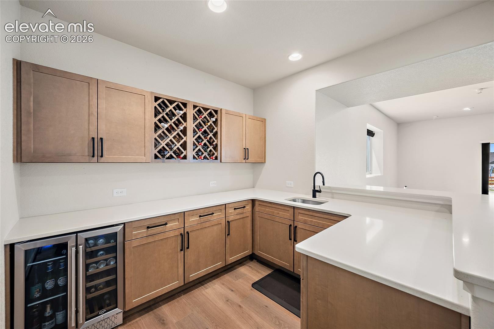 Built-in wet bar with solid surface countertops, a stainless steel wine refrigerator, under-mount sink, and wine storage