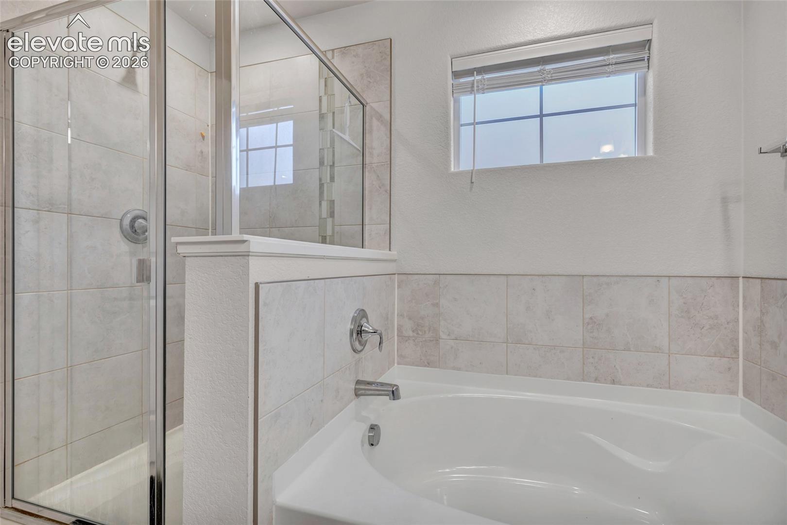 Walk-in shower with clear glass enclosure, tiled walls, and a separate soaking tub with chrome fixtures