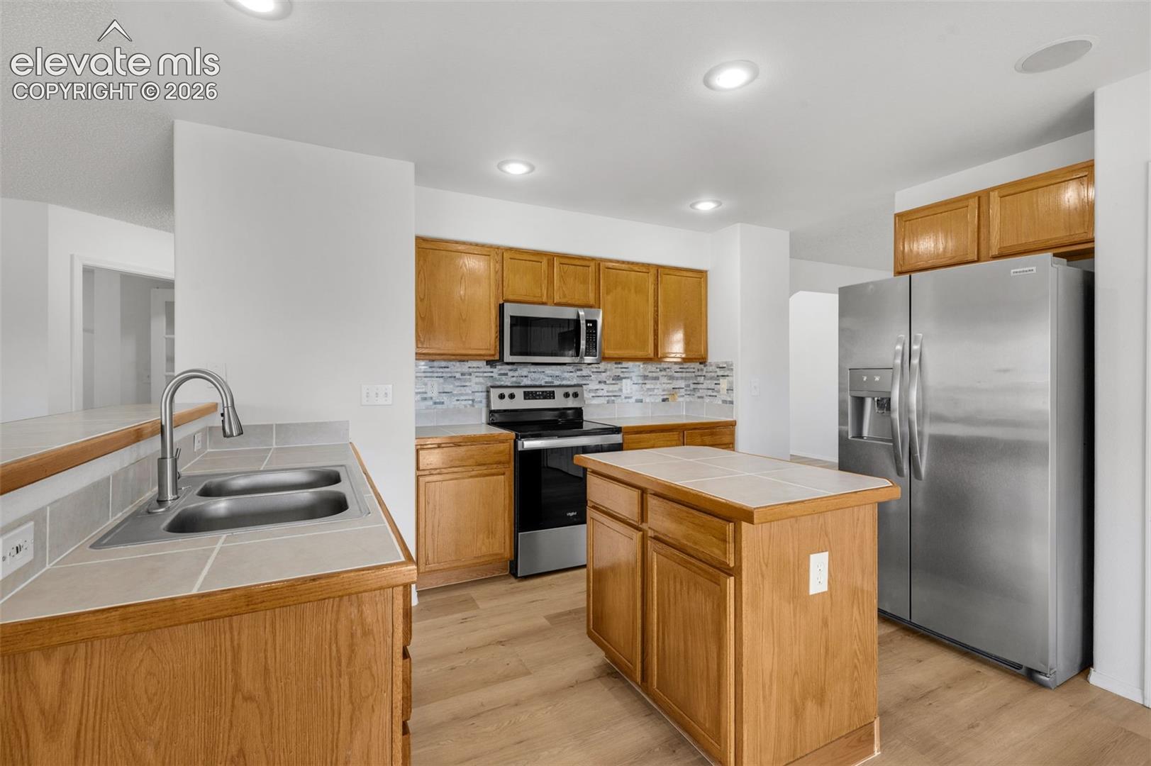 Kitchen featuring wood cabinetry, stainless steel appliances, a tiled backsplash, and wood-finish flooring