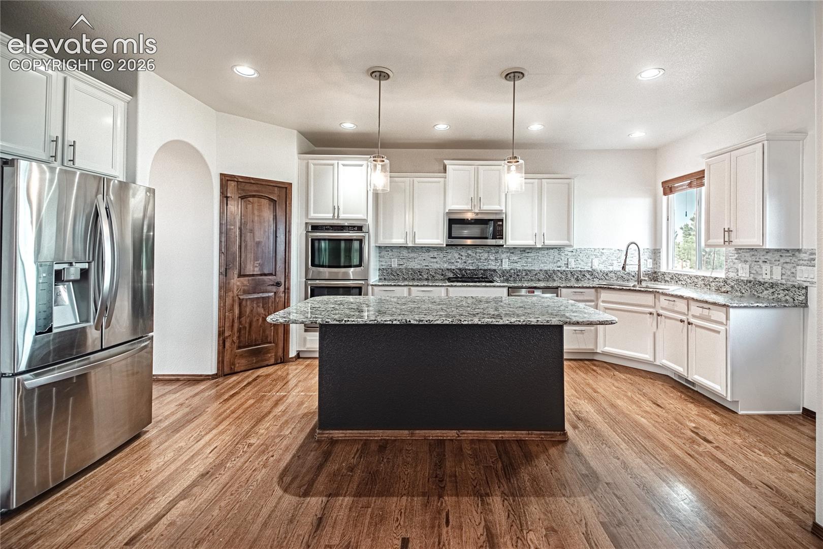 Kitchen featuring a large central island with a contrasting base, wood-finish flooring, white cabinetry, stainless steel appliances, and recessed lighting