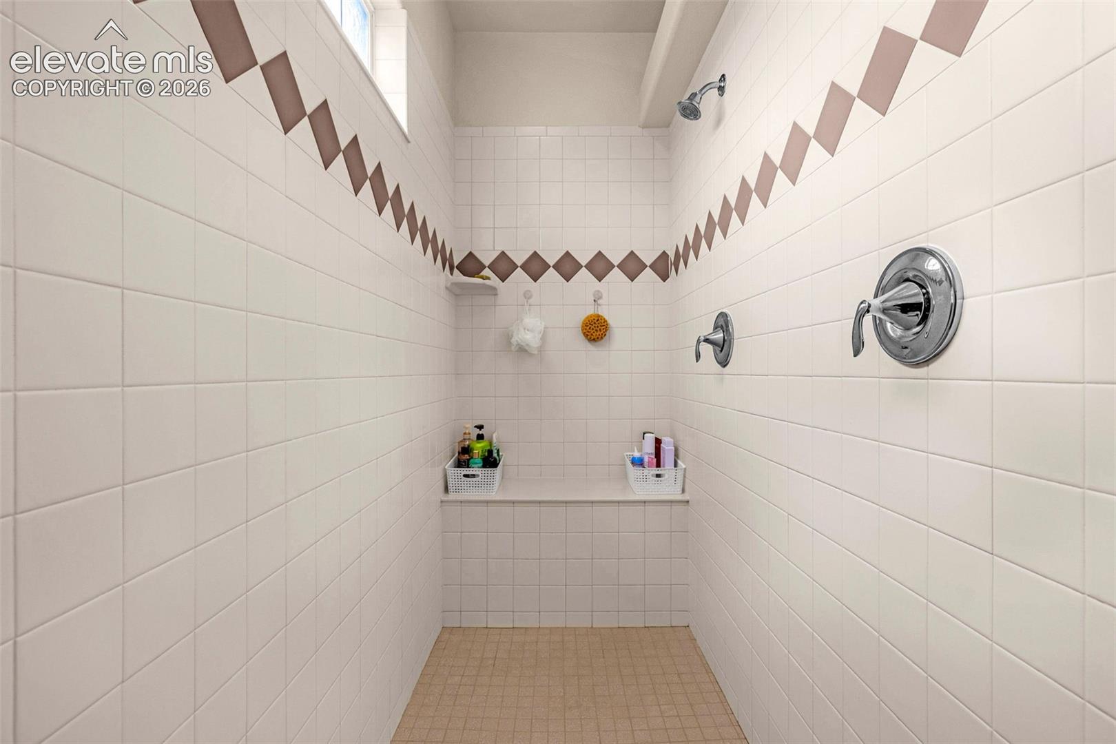 Walk-in shower featuring dual shower heads, built-in tiled bench seating, square tile wall surround with diamond-pattern accent tiling, and polished chrome fixtures