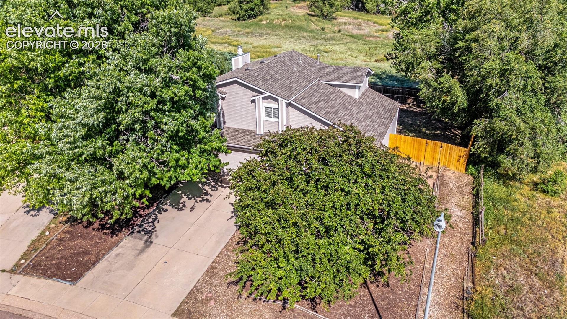 Two-story residence featuring composite shingle roofing, horizontal siding, concrete driveway, and natural wood privacy fencing situated on a lot with mature trees