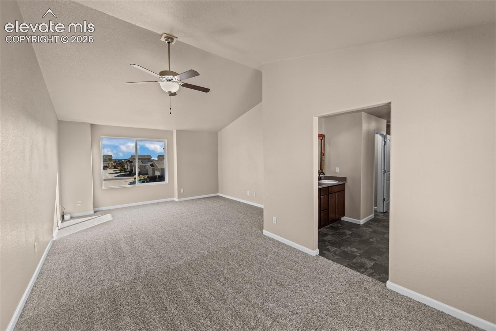 Vaulted ceiling, ceiling fan with light fixture, wall-to-wall carpeting, and large window
