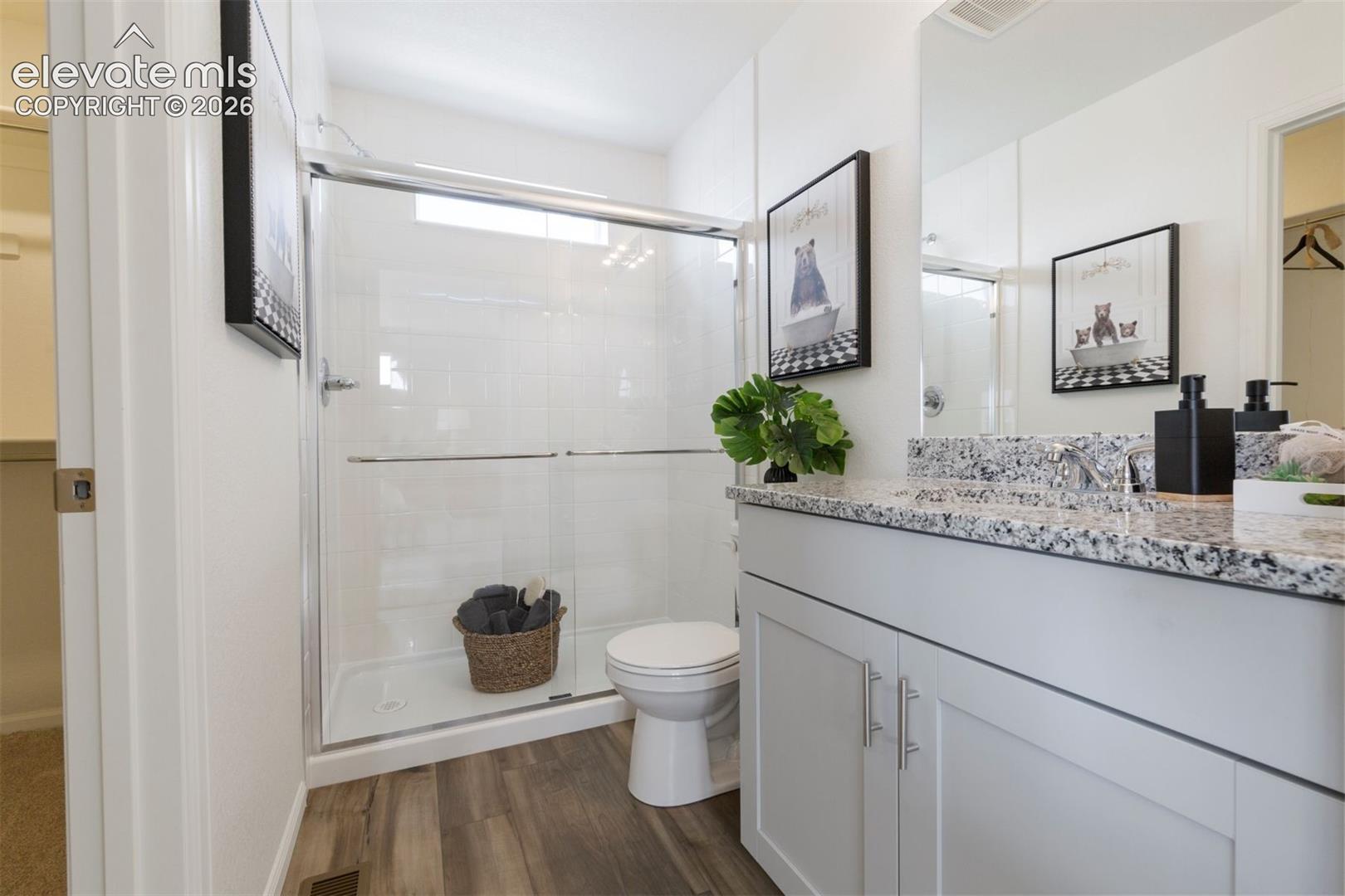 Walk-in shower with clear glass enclosure, single vanity with light-colored countertop, and wood-finish flooring
*photos of a model home*