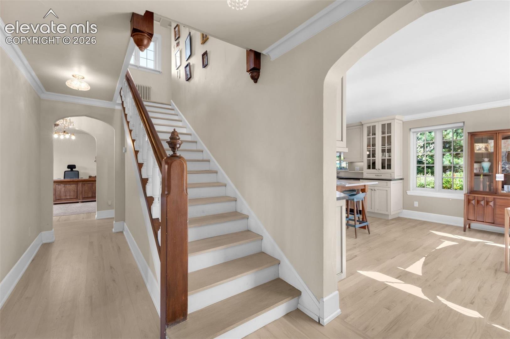 Staircase featuring wood-finish treads and a decorative wood newel post, architectural archways, and light-toned wood-finish flooring