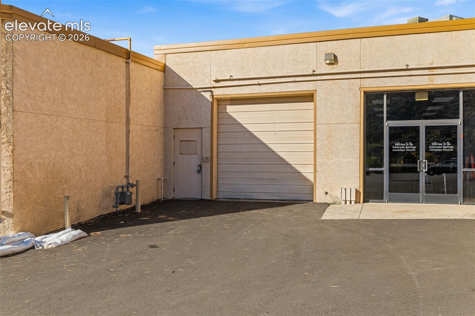Stucco exterior featuring a metal roll-up bay door, pedestrian side door, and dual-pane glass entry doors