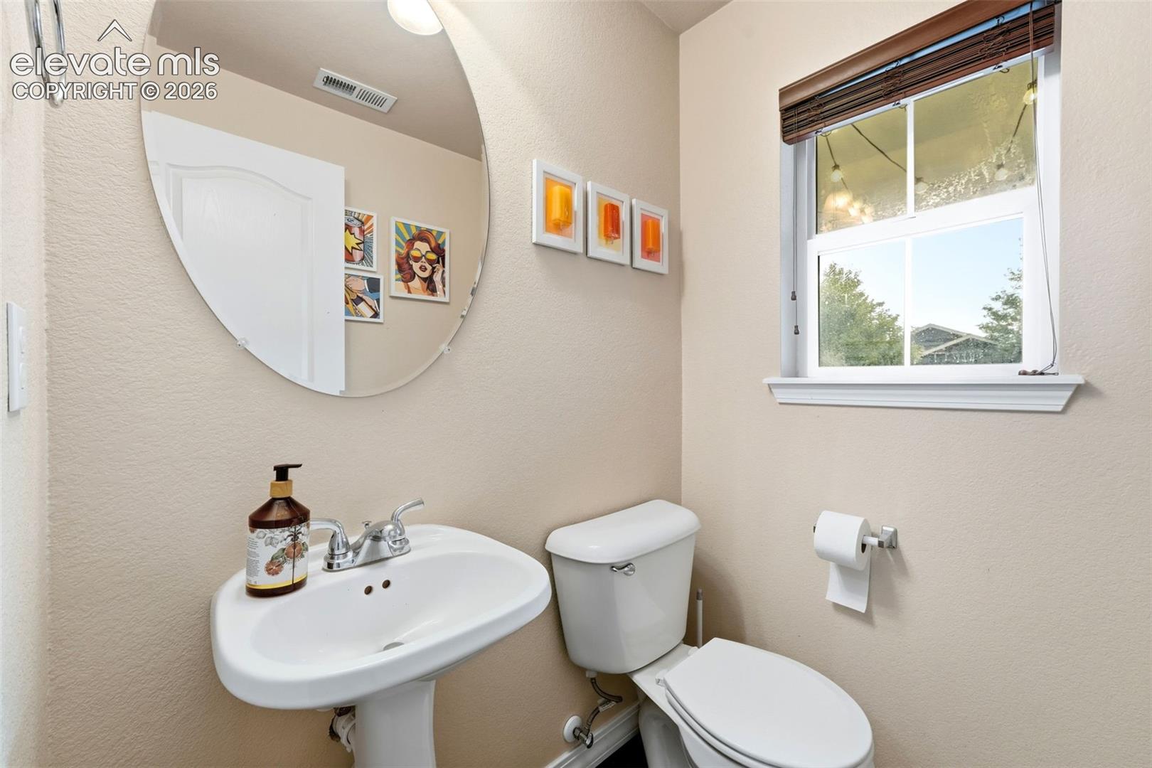Pedestal sink with chrome faucet, oval mirror, and a window with blinds