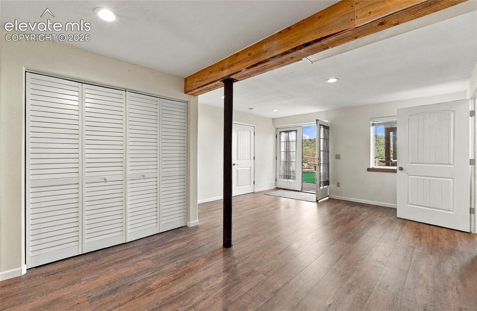 Wood-finish flooring, exposed natural wood ceiling beam, recessed lighting, white louvered closet doors, and French doors