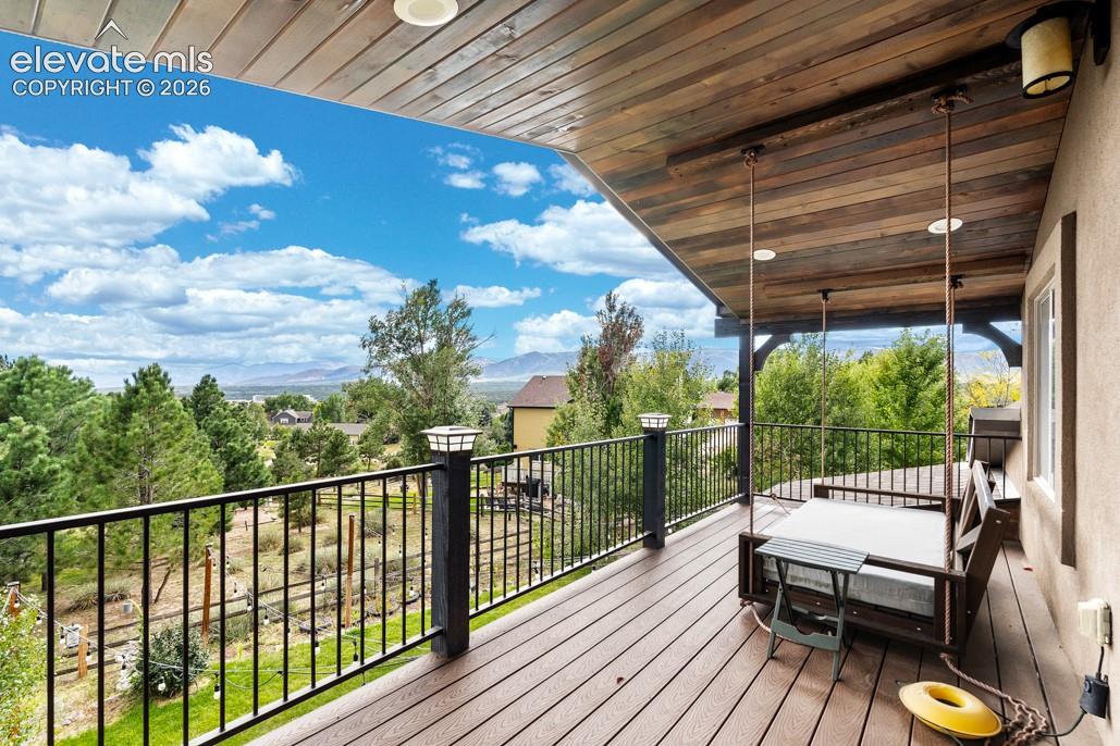 Expansive covered deck featuring wood-finish flooring, a wood-plank ceiling, and a wrought iron railing