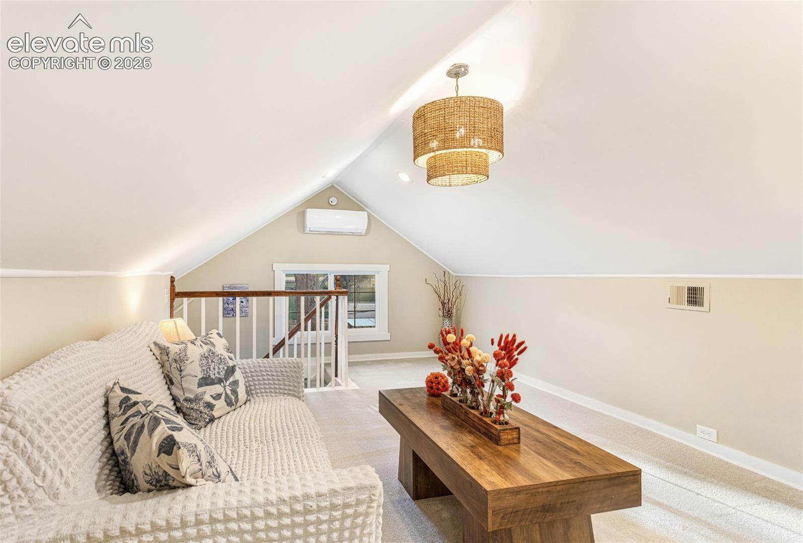 Vaulted ceiling loft space featuring a tiered woven chandelier, wall-mounted air conditioning unit, and plush neutral carpeting