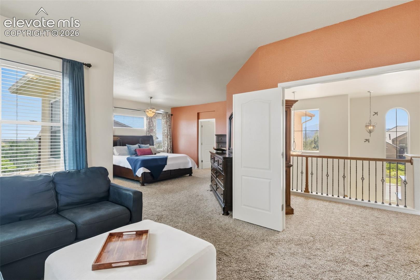 Carpeted bedroom space featuring a vaulted ceiling with an accent wall and multiple windows, firplace, french doors