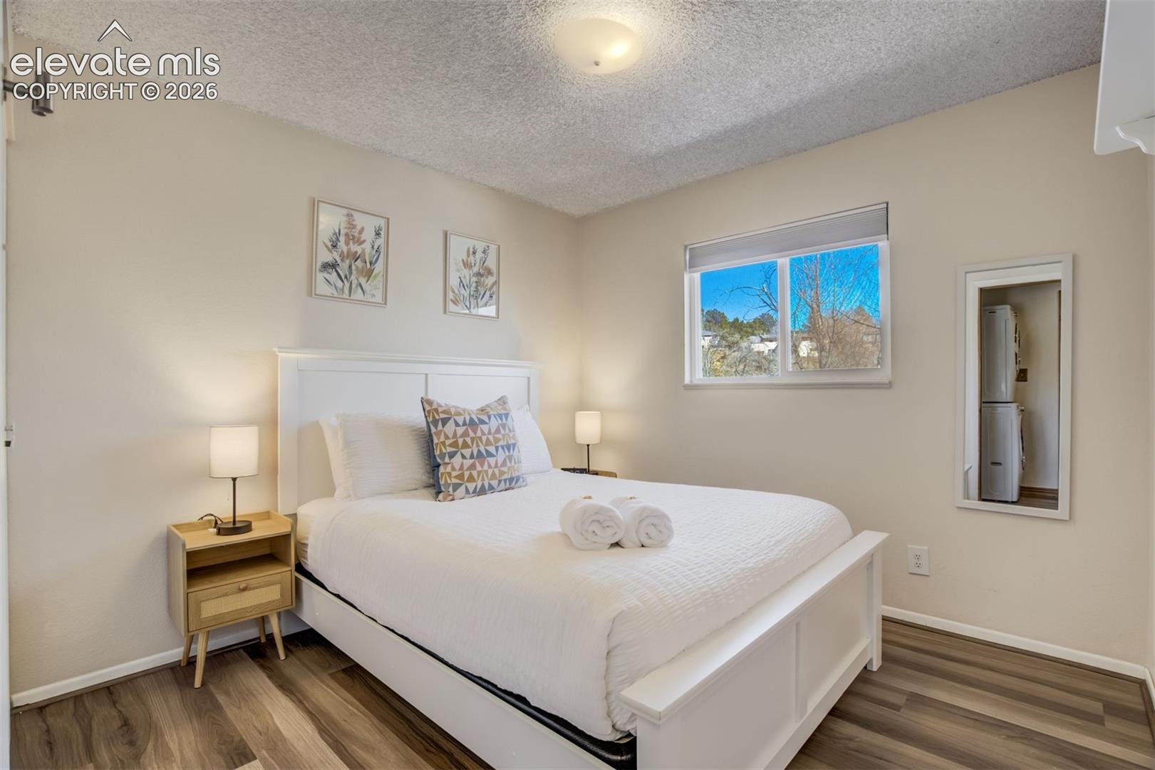 Recessed window with roller shade, wood-finish flooring, and neutral wall paint