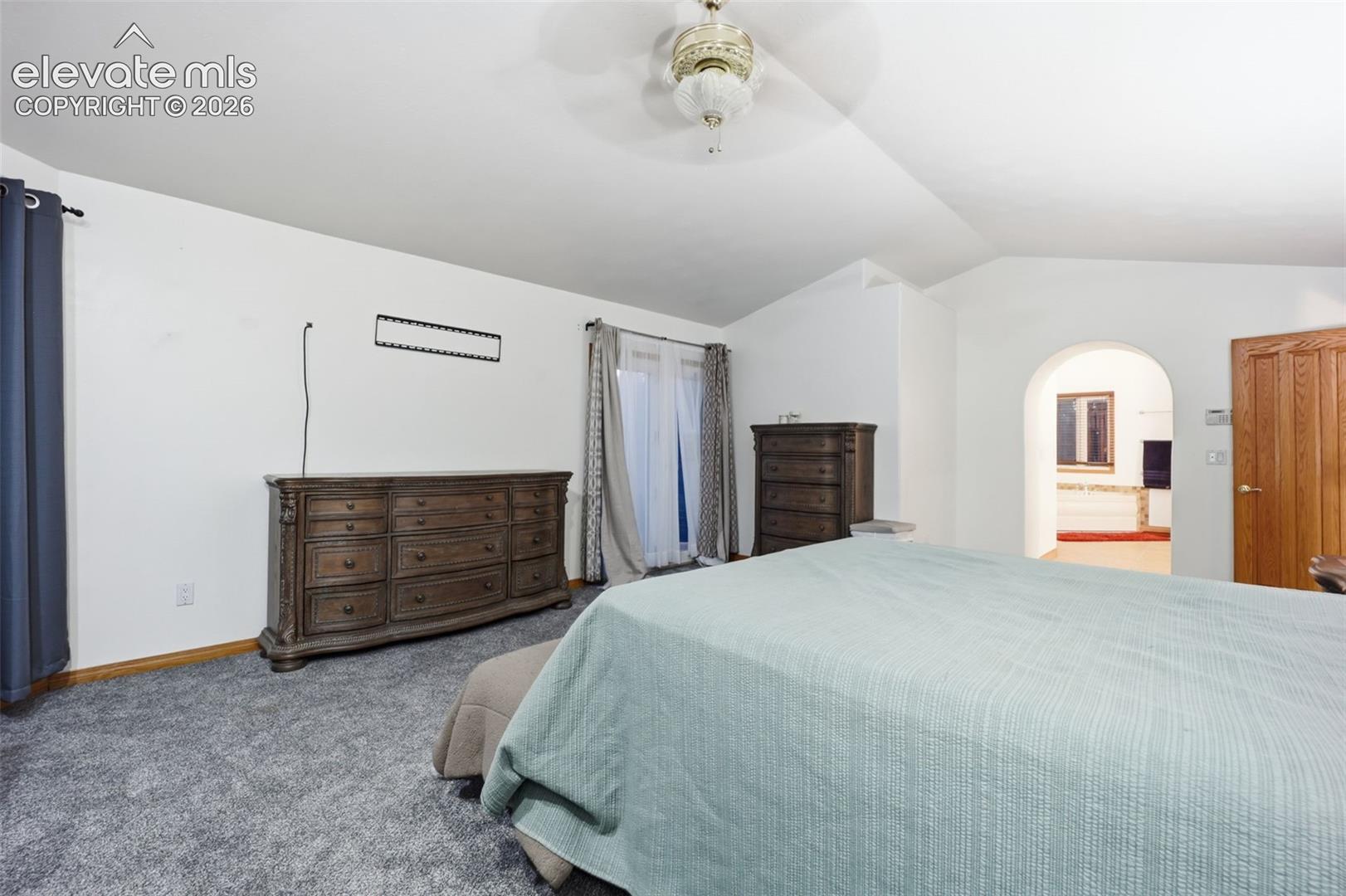 Carpeted flooring, vaulted ceiling, arched doorway, and a wood-panel door
