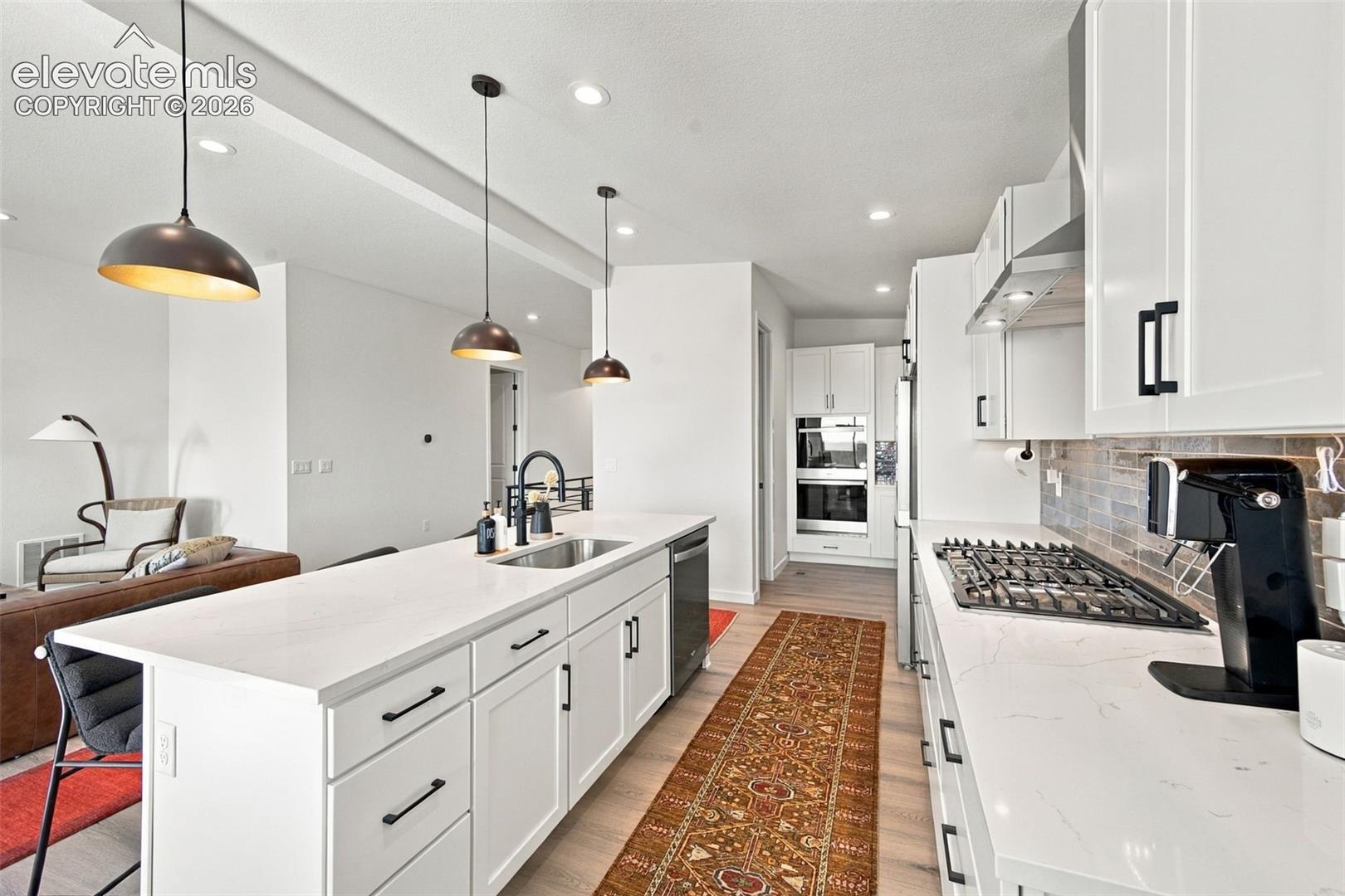 Kitchen featuring white shaker-style cabinetry, quartz countertops, a gas cooktop, built-in double wall ovens, and three pendant lights