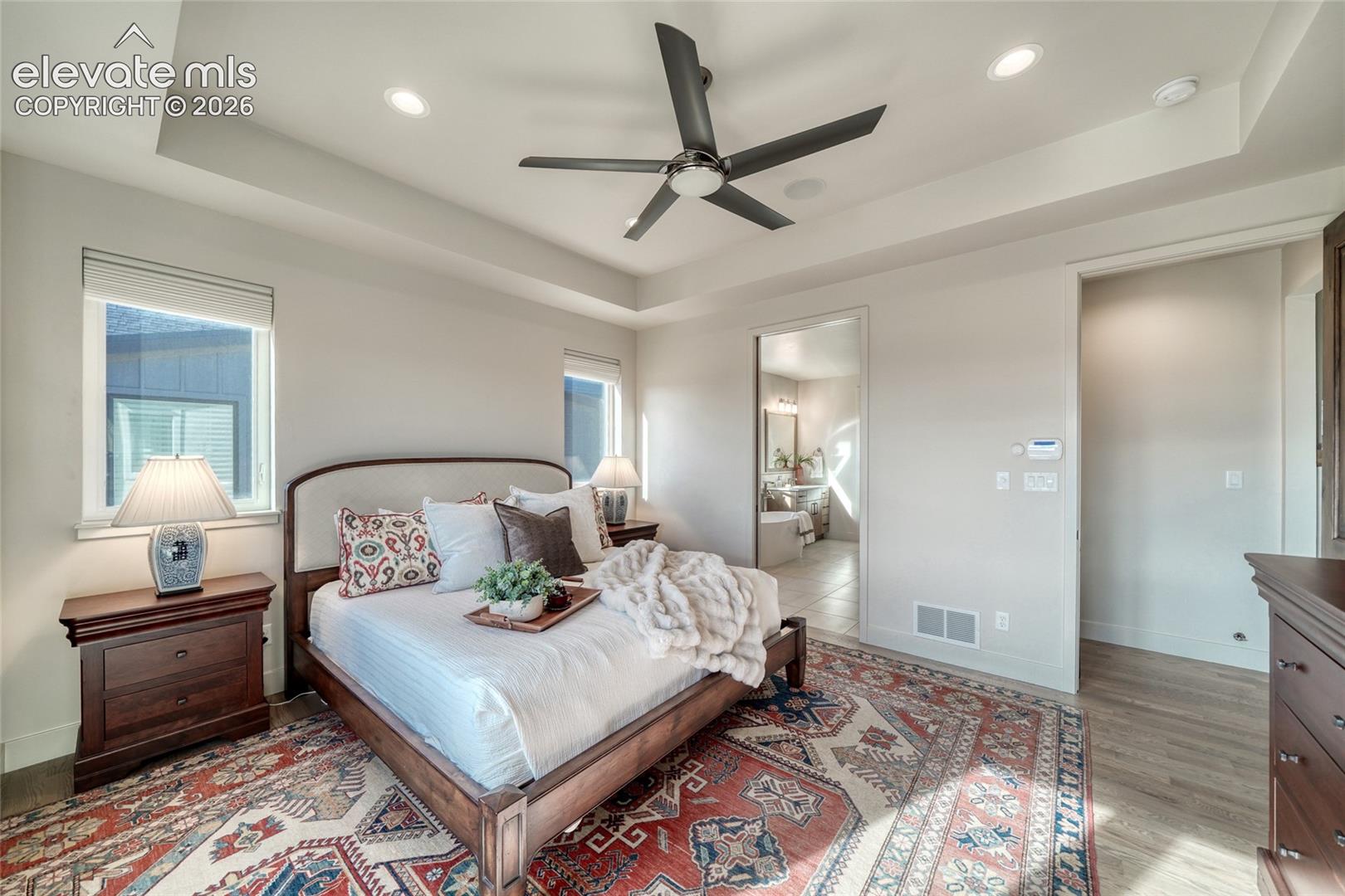 Tray ceiling with recessed lighting and a central ceiling fan, paired with wood-finish flooring