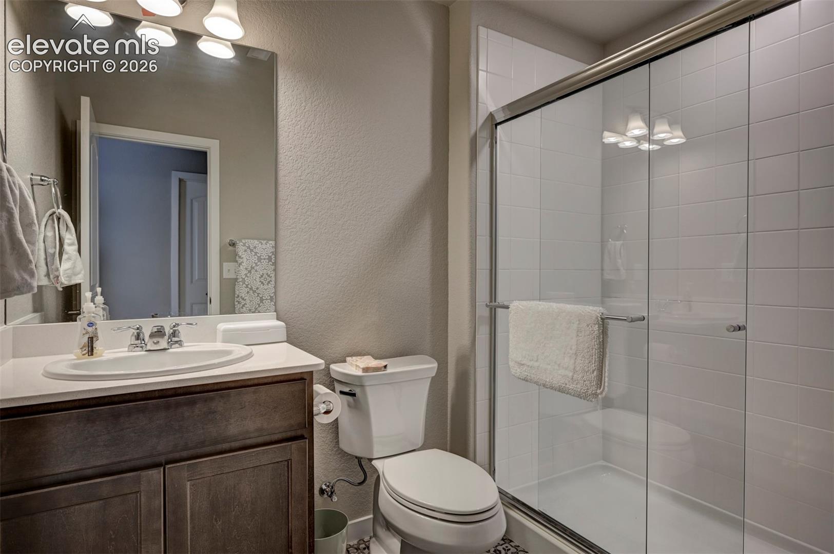 Bathroom featuring a wood-finish vanity, white countertop, oval sink, large wall-mounted mirror, and a glass-enclosed shower with white subway tile