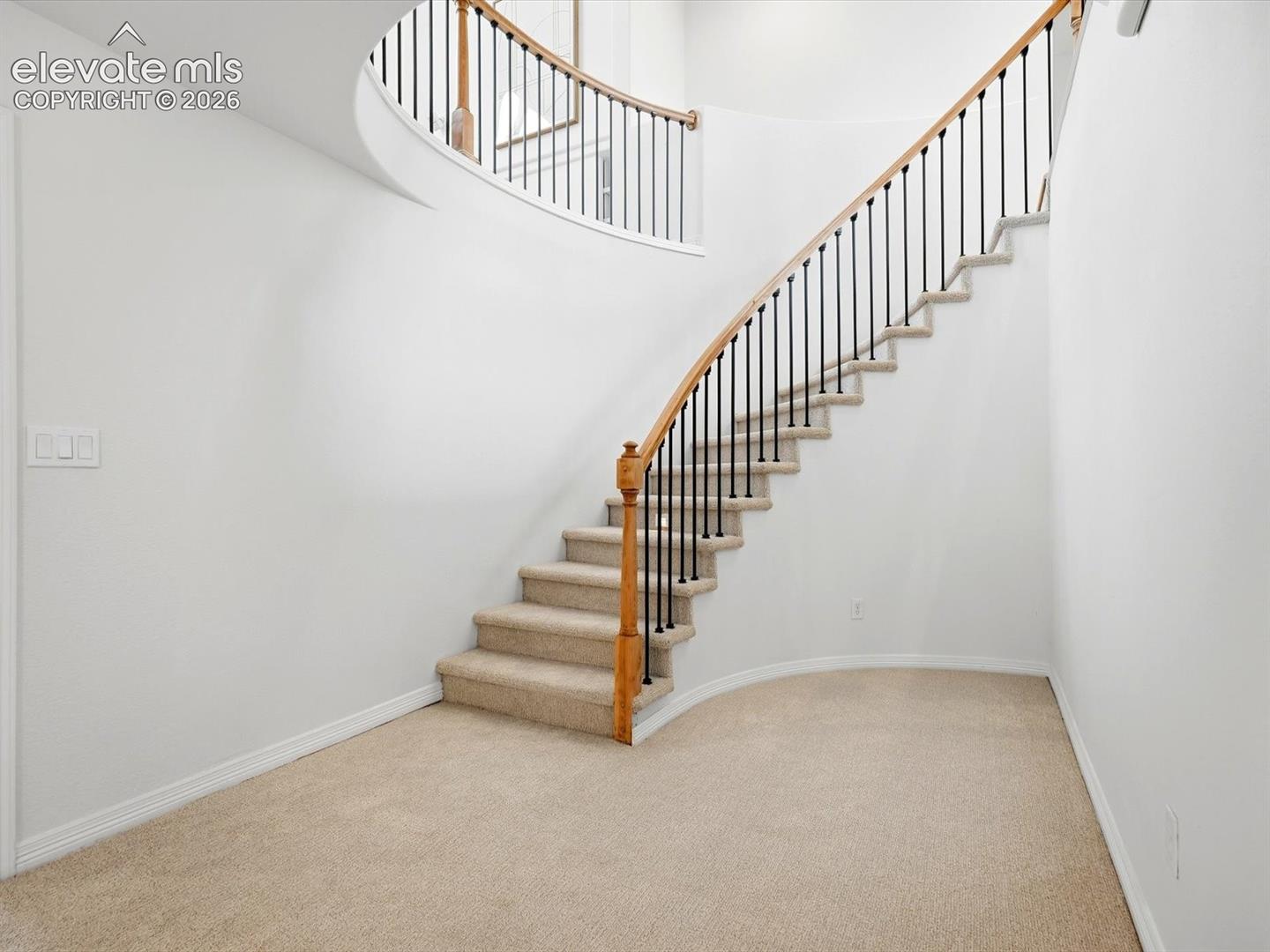 Curved staircase featuring carpeted treads, a wooden handrail, and black metal balusters