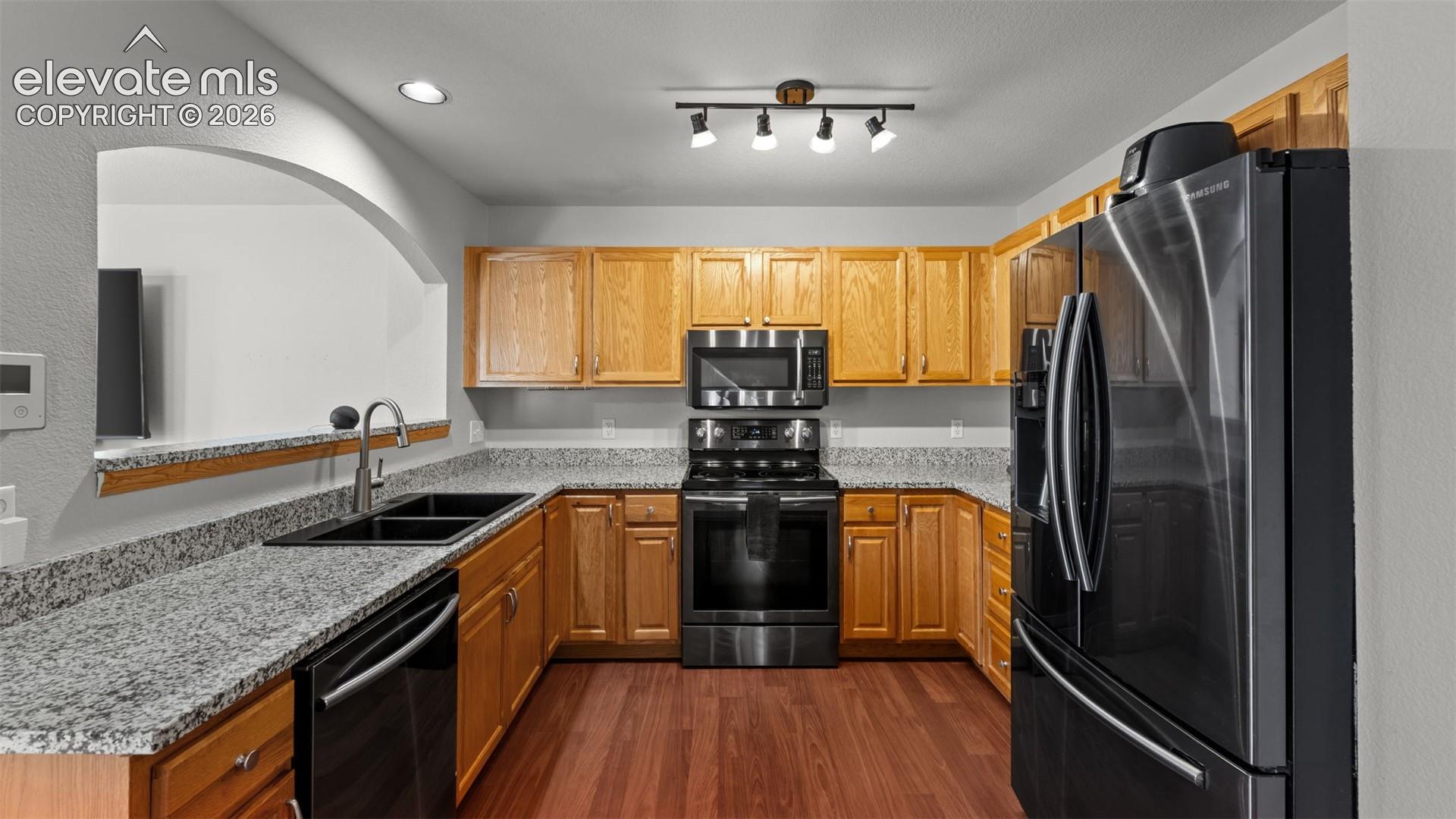 Kitchen featuring natural wood cabinetry, stone-finish countertops, black finish appliances, wood-finish flooring, and a decorative arched wall cutout