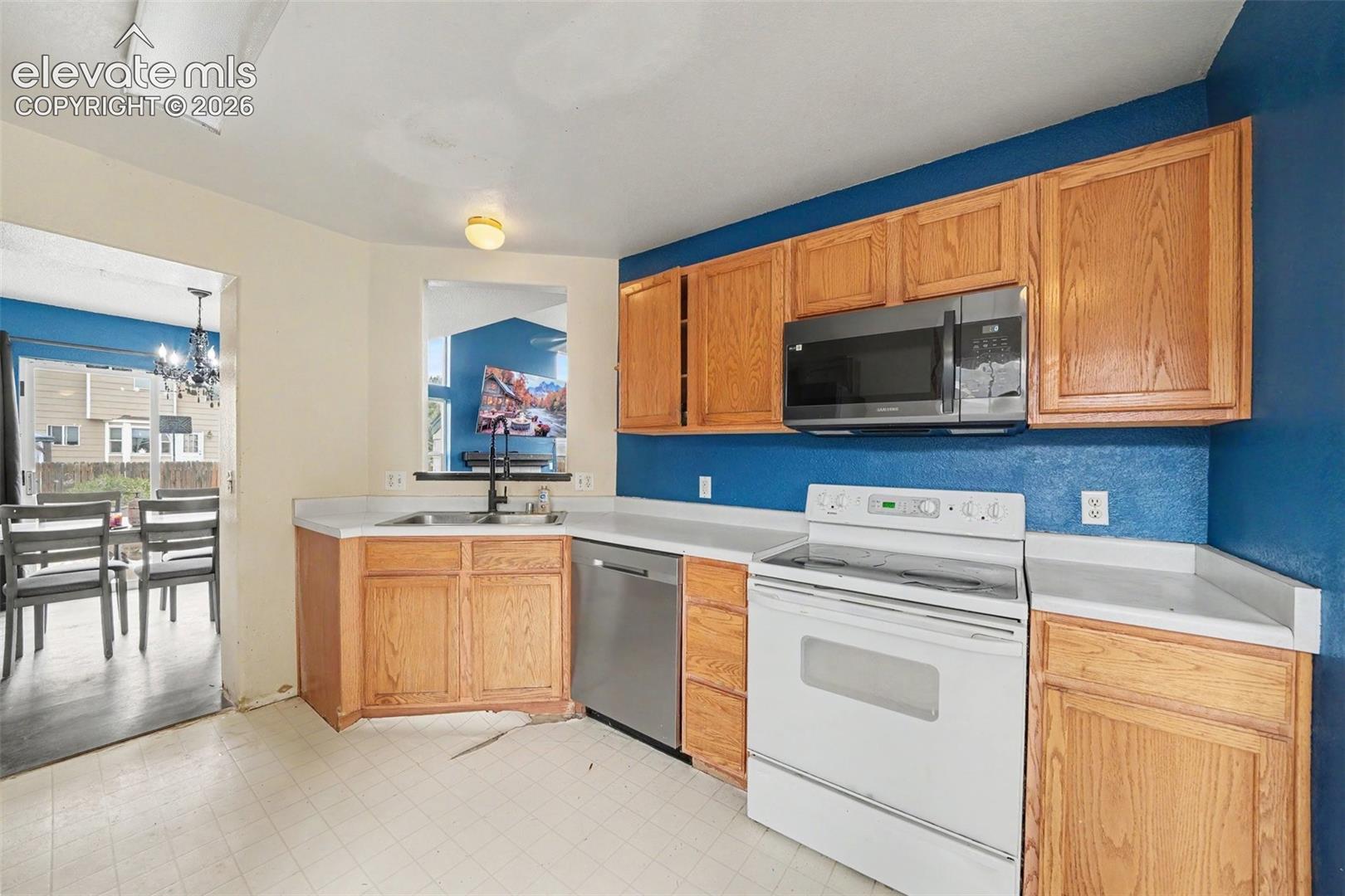 Kitchen featuring wood cabinetry, stainless steel dishwasher, built-in microwave, white range, and a pass-through window above the sink