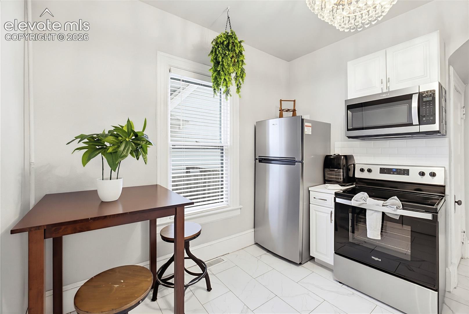 Kitchen featuring stainless steel appliances, white subway tile backsplash, white cabinetry, and a crystal chandelier