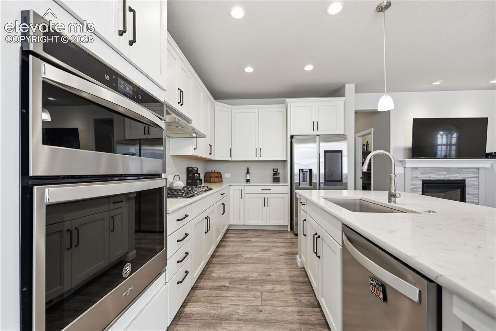Kitchen featuring white cabinetry, stainless steel appliances, light  brown luxury vinyl plank flooring, recessed lighting, and a kitchen island with an undermount sink.