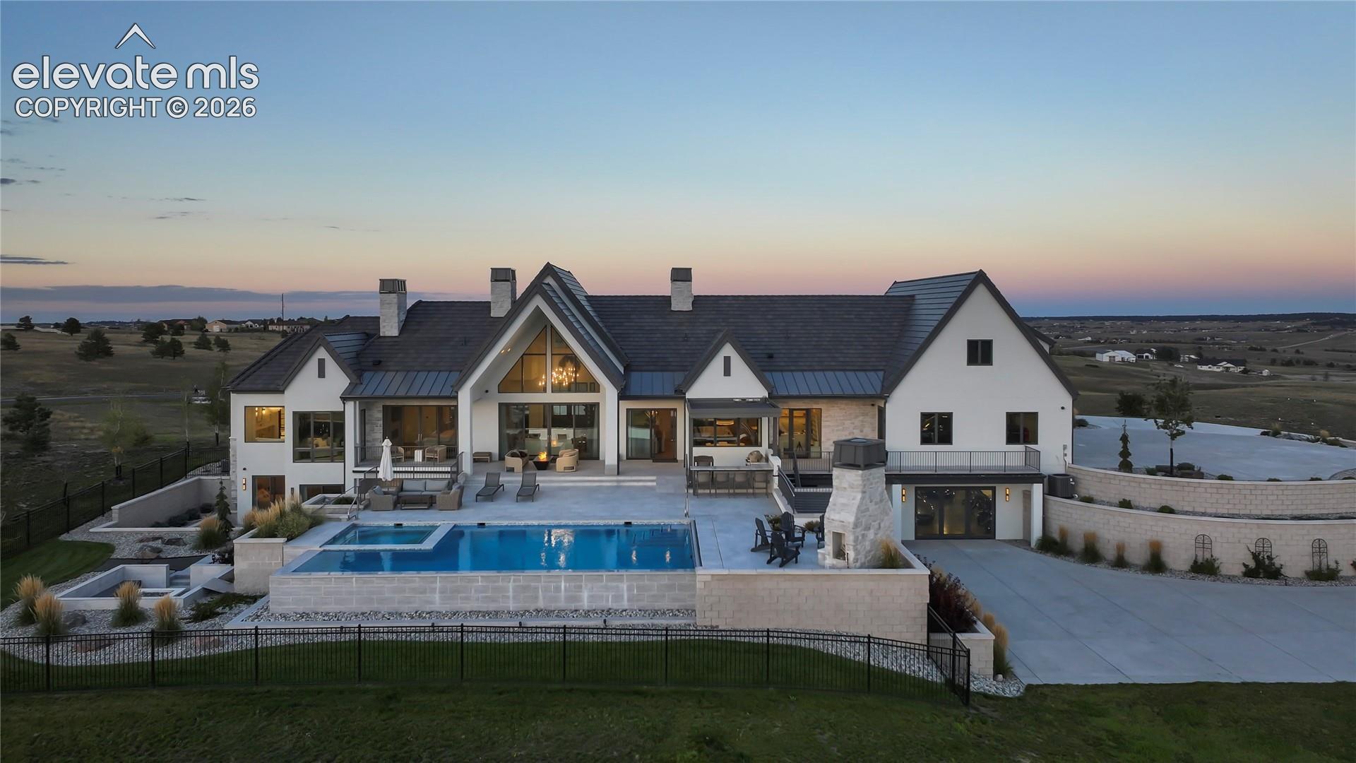 Stucco and stone exterior featuring a multi-gabled roofline, an infinity-edge pool, an integrated spa, and a custom stone outdoor fireplace