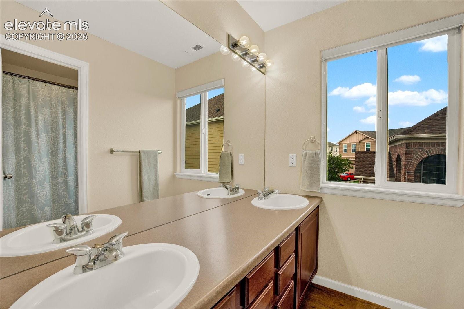 Double vanity featuring integrated sinks, solid-surface countertop, dark wood-finish cabinetry, and a full-width mirror